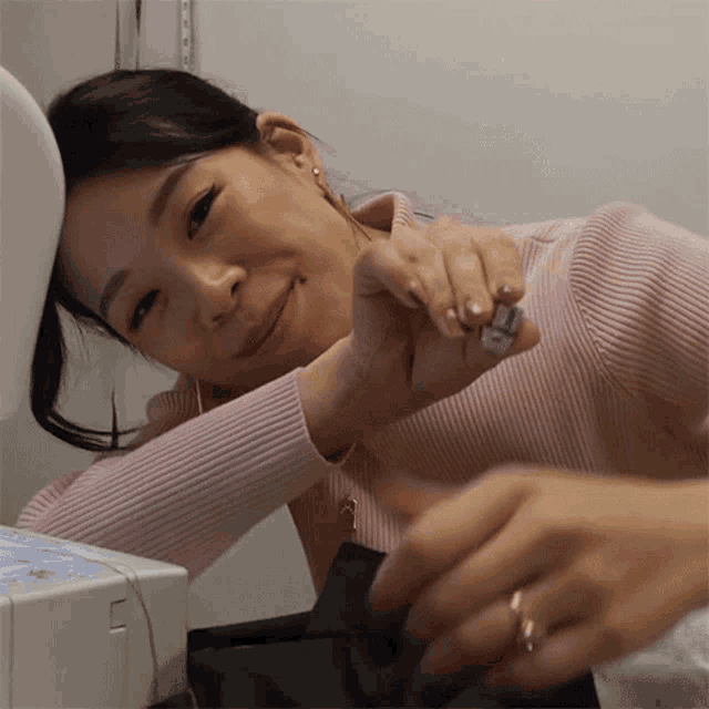 a woman in a pink sweater is working on a sewing machine and smiling