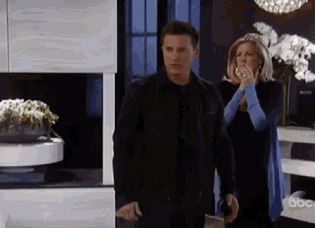 a man and a woman are standing in a living room . the woman is covering her mouth with her hand .