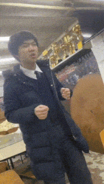 a man in a black jacket and tie stands in front of a shelf with trophies on it