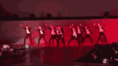 a group of people are dancing on a stage in front of a pink background .