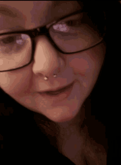 a woman wearing glasses and a nose ring makes a face