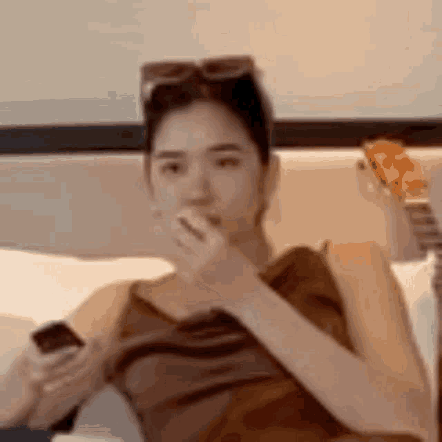 a woman is sitting on a bed holding a cell phone in her hand and covering her mouth .