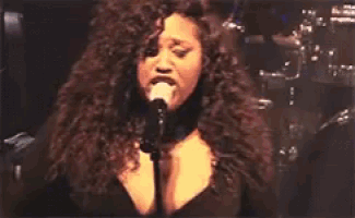 a woman singing into a microphone with her hands on her head .