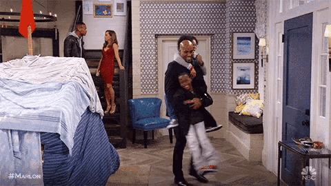 a man is holding a child in his arms in a living room while a woman stands in the background .