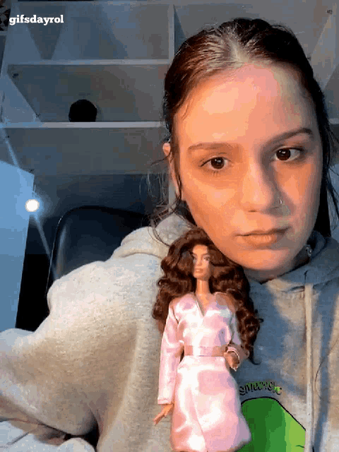 a girl is holding a barbie doll and wearing a sweatshirt that says snuggle