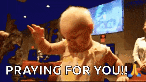 a baby is praying for you while sitting in front of a large screen