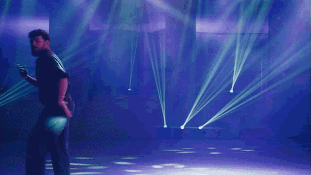 a man in a black shirt is dancing in a dark room with purple lights behind him