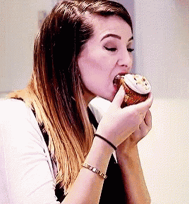 a woman is eating a cupcake with frosting and sprinkles on it .