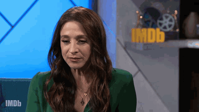 a woman in a green jacket sits in front of an imdb logo