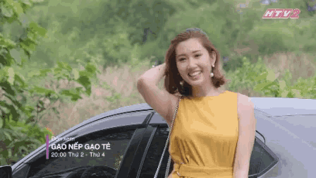 a woman in a yellow dress is standing in front of a car that says " gao nep gao te " on it
