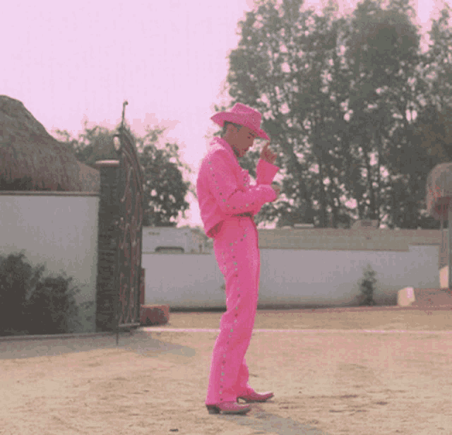 a man in a pink suit and cowboy hat is standing in a dirt field