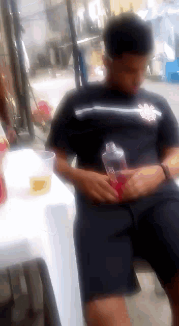 a man in a black shirt is sitting at a table holding a bottle of soda .
