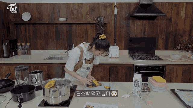 a woman in an apron is cooking in a kitchen with a twice logo on the wall