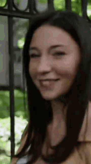a close up of a woman 's face smiling in front of a wrought iron fence .