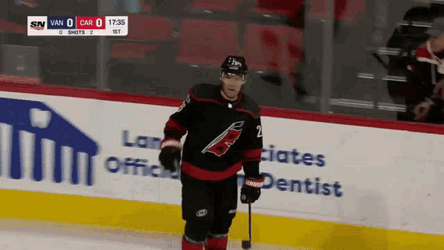 a hockey player stands on the ice with a puck in front of an ad for a dentist