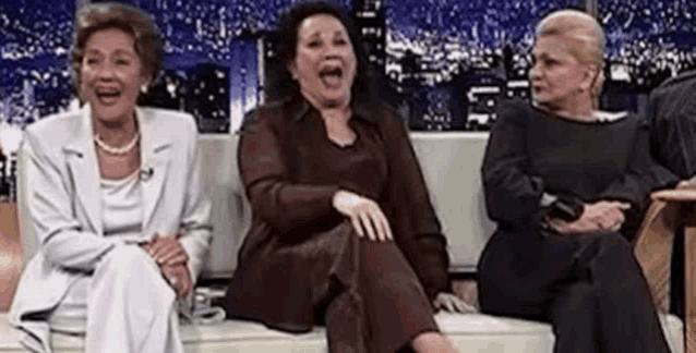 three older women are sitting on a couch laughing together .