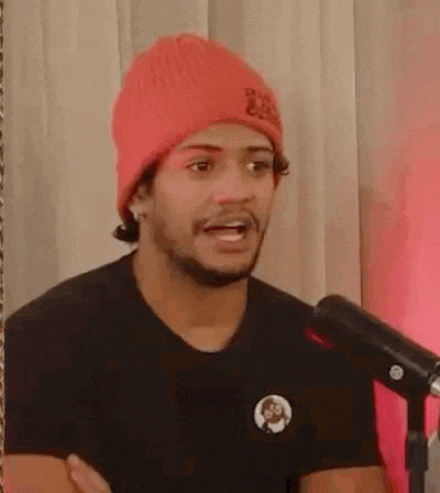 a man wearing a red beanie and a black shirt is sitting in front of a microphone with his arms crossed .