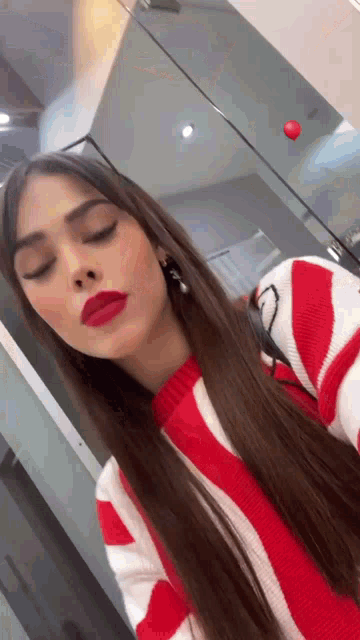 a woman wearing a red and white striped sweater is taking a selfie with her eyes closed .