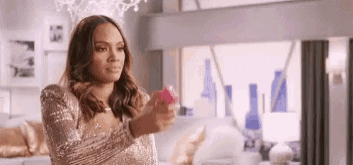 a woman in a sequined dress is standing in a living room holding a pink object .