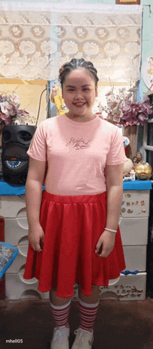 a girl wearing a pink shirt and red skirt is smiling