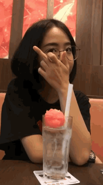 a woman covering her face with her hand while sitting at a table with a glass of water
