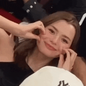 a woman is making a heart shape with her hands on her face while smiling .