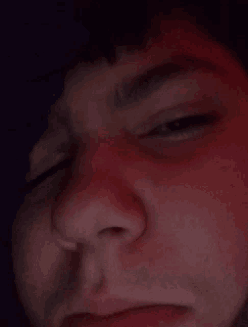 a close up of a man 's face with his eyes closed and a red background .