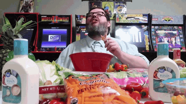 a man is eating carrots in front of an arcade with mortal kombat on the screen