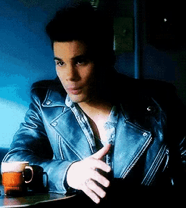 a man in a blue leather jacket is sitting at a table with a cup of coffee and a mug that says california