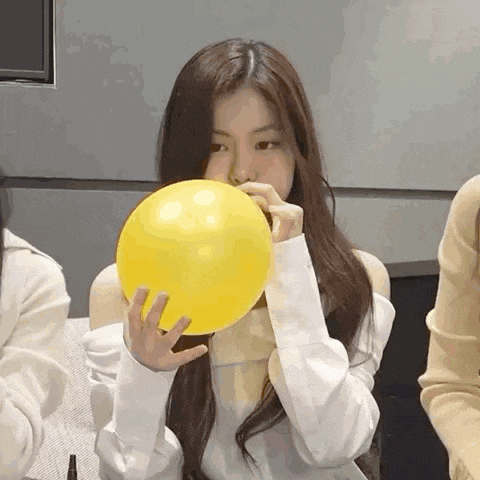 a woman is blowing up a yellow balloon in her hand .