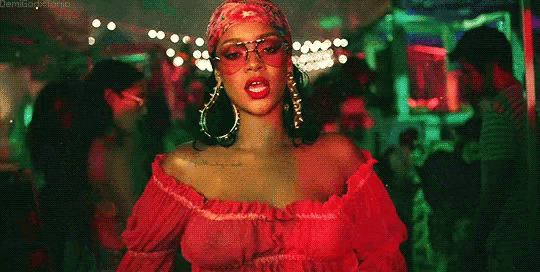 a woman in a red off the shoulder top and sunglasses is standing in a crowded room .