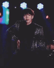 a man in a sequined jacket is singing into a microphone on a stage