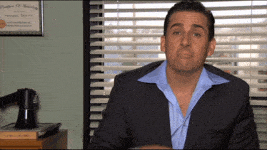 a man in a suit is sitting in front of a window with blinds and a certificate that says michael scott