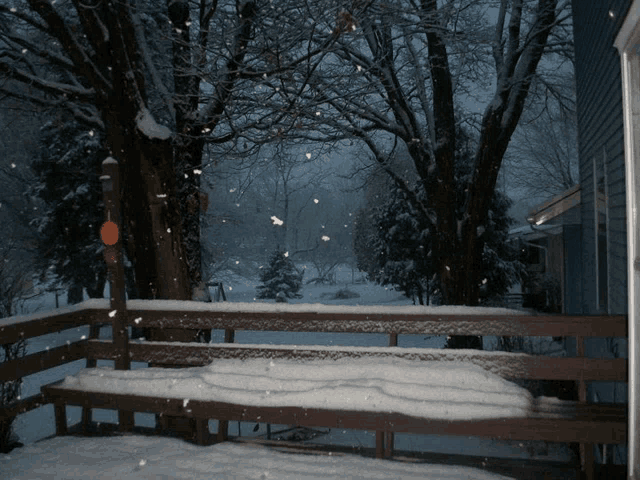 a snowy deck with trees in the background and snow falling