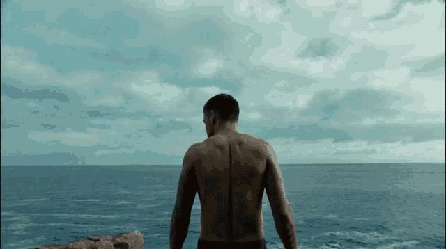 a man without a shirt is standing on a cliff overlooking the ocean