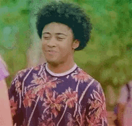 a young man with curly hair is wearing a purple shirt with a floral pattern .