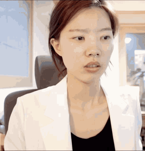 a woman with a nose ring is wearing a white jacket and black shirt