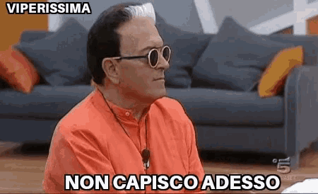 a man wearing sunglasses is sitting in front of a couch and says non capisco adesso