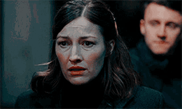 a woman is looking at the camera with a man behind her .
