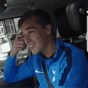 a man in a blue nike jacket is smiling while sitting in a car