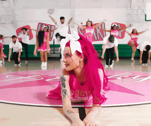 a cheerleader with pink hair is kneeling on the floor in front of a sign that says ' sr '