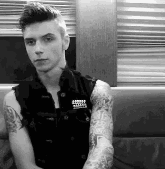 a young man with a lot of tattoos on his arms is sitting on a couch .