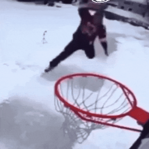 a person is playing basketball in the snow with a red hoop .