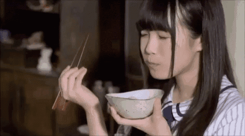 a girl is eating rice with chopsticks from a bowl .