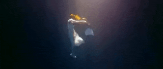 a man and woman are dancing underwater in the dark .