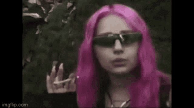 a woman with pink hair wearing sunglasses and smoking a cigarette .