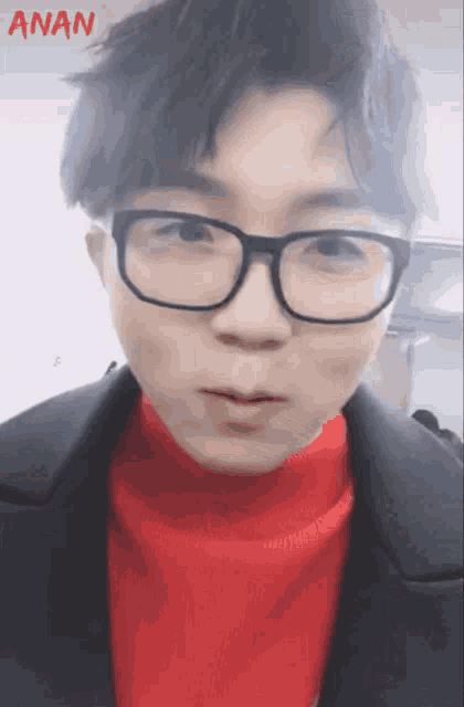 a young man wearing glasses and a red sweater has the word anan above him