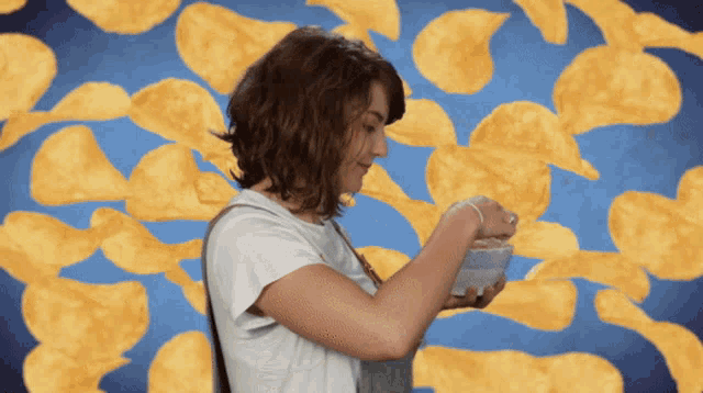 a woman is eating a bowl of chips in front of a pile of chips