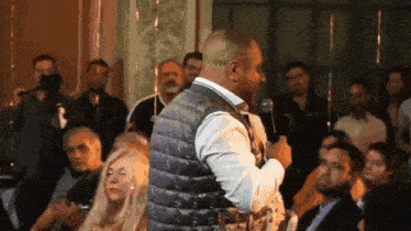 a man in a purple vest is speaking into a microphone