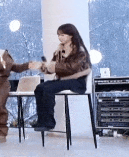 a woman is sitting in a chair holding a microphone while another woman stands behind her .